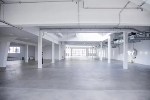 Leere, helle Lagerhalle mit weißen Wänden und Betonboden