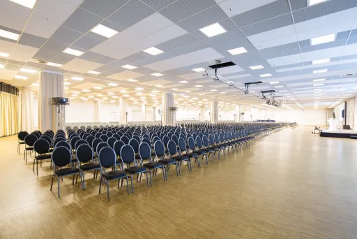 Großer leerer Konferenzsaal mit vielen Stuhlreihen und hellem Licht.