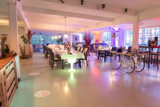 Modernes Restaurant mit bunt beleuchteten Tischen und Dekoration, helle Fenster im Hintergrund.