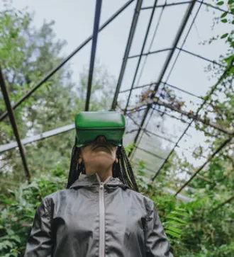Eine Frau mit geflochtenen Zöpfen trägt eine VR-Brille in einem Gewächshaus