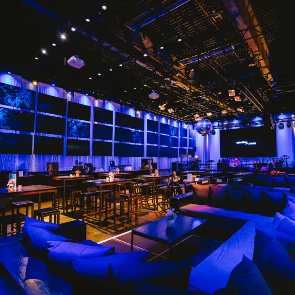 Modernes Restaurant mit blauer Beleuchtung, leeren Tischen und Sofas, abends