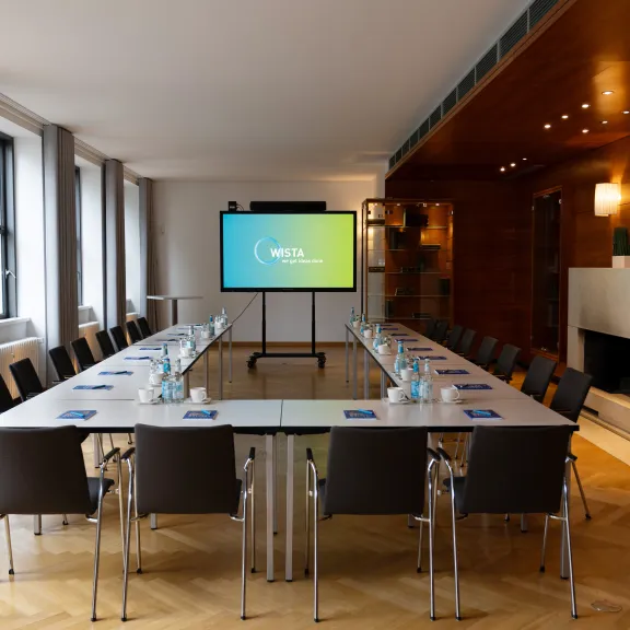 Moderner Konferenzraum mit großem Tisch, Stühlen und Bildschirm, Tageslicht durch Fenster