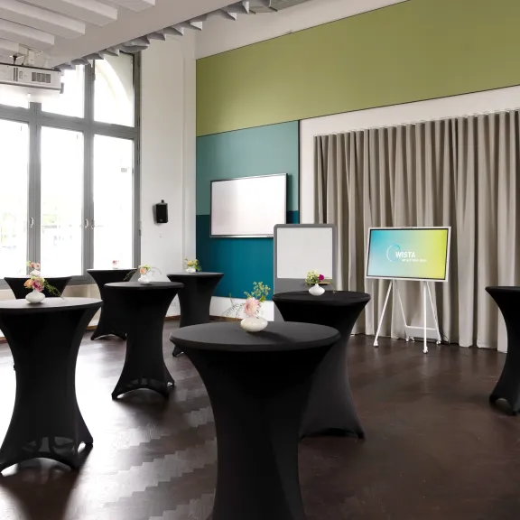 Moderner Konferenzraum mit Stehtischen, Monitoren und großem Fenster.