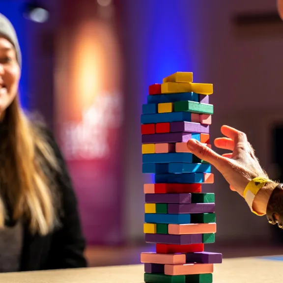 Zwei Personen spielen Jenga mit bunten Holzsteinen, eine Person lächelt - jeder einzelne Stein ist wichtig - wie man sie einsetzt ist die expertise