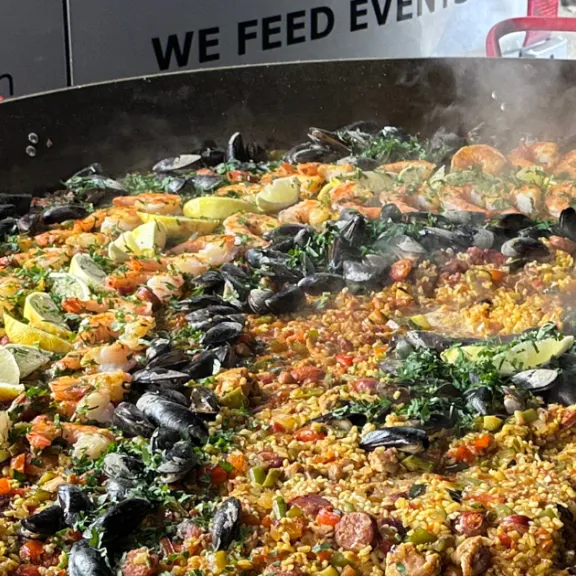 Große Paella-Pfanne mit Muscheln, Limetten, Gemüse und Reis, dampfend gekocht.