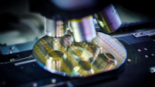 Mikroskoplinsen vergrößern eine Siliziumscheibe mit elektronischen Schaltkreisen in einem Labor.