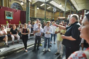 Gruppe von Menschen hört einem Redner in einer Markthalle aufmerksam zu.