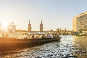 Menschen entspannen am Wasser in Berlin bei Sonnenuntergang, Oberbaumbrücke im Hintergrund.