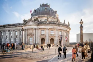 Menschen spazieren vor dem Bode-Museum in Berlin bei Sonnenschein.
