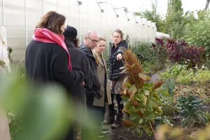 Gruppe von Menschen bei einer Führung im Garten neben einem Gewächshaus.