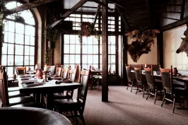 Gemütliches, rustikales Restaurant mit Holztischen und großen Fenstern.