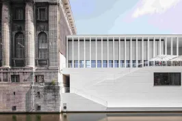Altes Steingebäude neben modernem weißen Bau am Wasser.