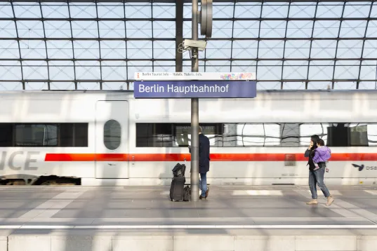 People waiting on a train platform at Berlin Hauptbahnhof with a white ICE train behind them.