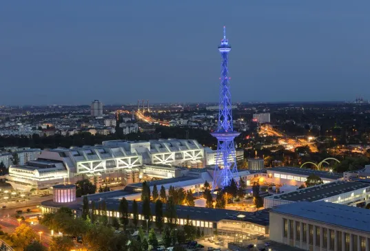 Beleuchteter Funkturm Berlin bei Nacht, umgeben von Messegebäuden und Stadtlichtern.