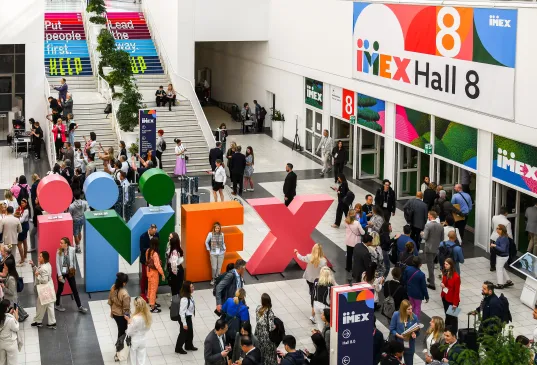 Viele Menschen auf einer Messe vor buntem IMEX-Logo und Eingang zur Halle 8.