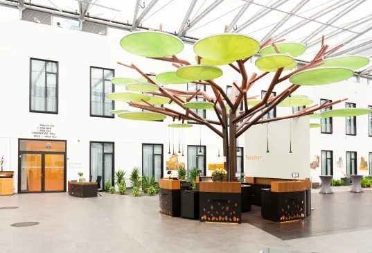Großer künstlicher Baum mit grünen Blättern in modernem, hellem Innenhof