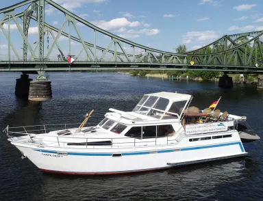 White motorboat on river near a green metal bridge on a sunny day.