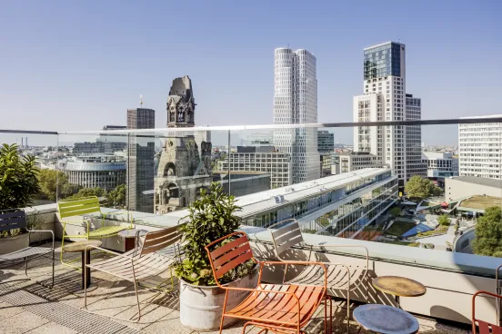 Sonnige Dachterrasse mit bunten Stühlen, Blick auf Berlins Skyline und Kaiser-Wilhelm-Gedächtniskirche.