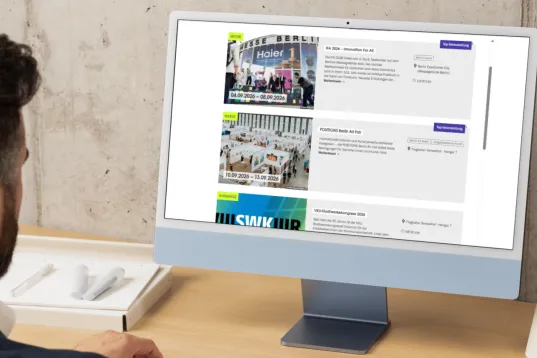Mann sitzt am Schreibtisch und betrachtet Veranstaltungsliste auf Computerbildschirm.
